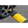 Roue de voiture franchissant un ralentisseur de sécurité noir et jaune de 5 cm sur une chaussée en asphalte.