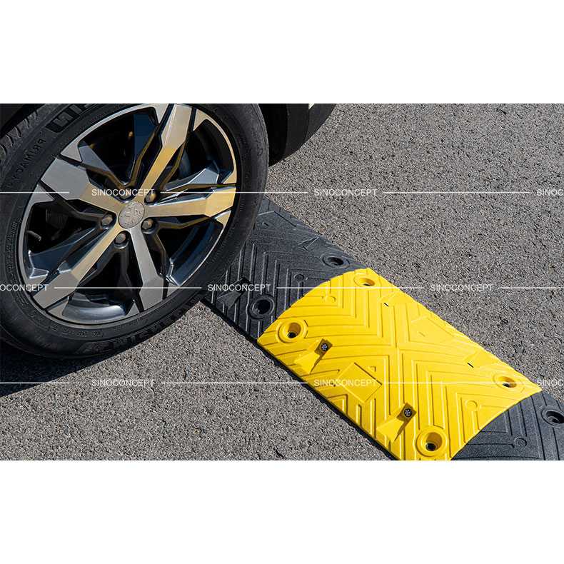 Roue de voiture franchissant un ralentisseur de sécurité noir et jaune de 5 cm sur une chaussée en asphalte.