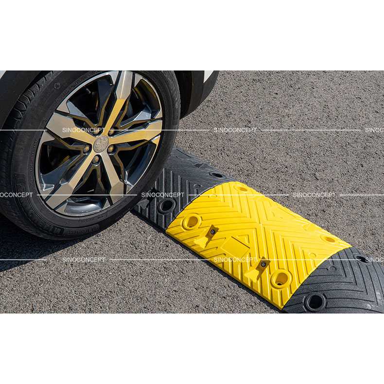 Roue de voiture franchissant un ralentisseur de sécurité noir et jaune de 7 cm sur une chaussée en asphalte.